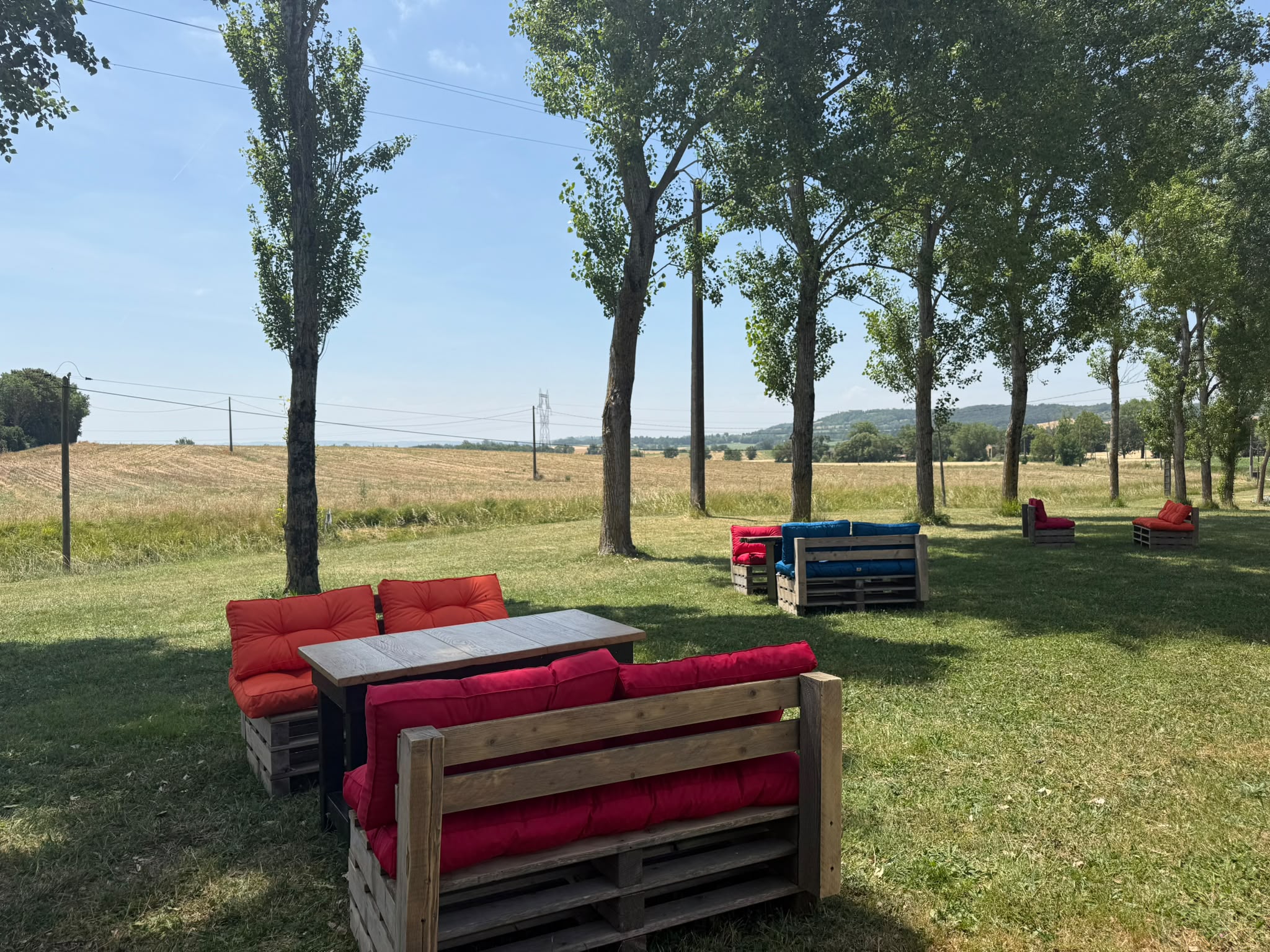 Salons en palettes et coussins colorés sous les arbres face à la campagne